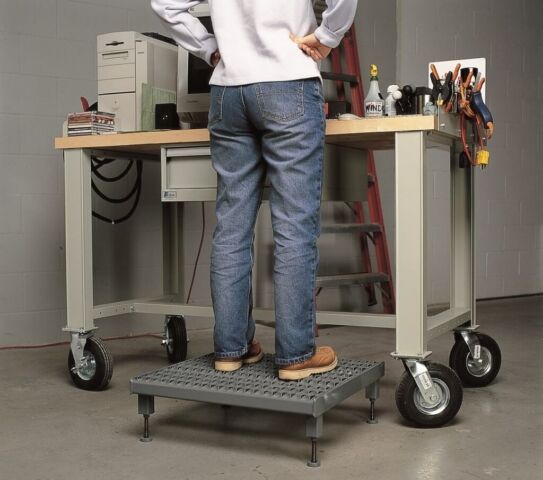 Person standing on an one step adjustable height work platform at a workstation